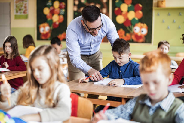 istock Young happy professor assisting his elementary students on a class at school. 1433288732