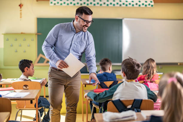 istock Happy male teacher assisting his student on a class at elementary school. 1433288757
