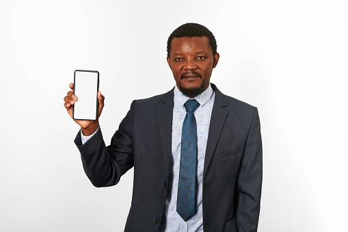 African american black man in business suit with smartphone blank mockup in hand, white wall background. Portrait of black businessman holding white phone mock up for advertising