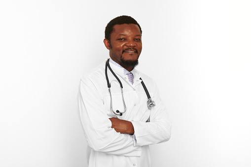 Smiling black bearded doctor man crossed arms in white coat with stethoscope isolated on white background. Adult black african american physician therapist portrait, confident candid male emotion