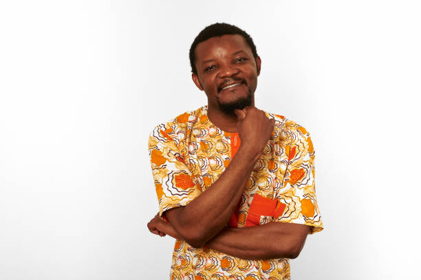 Thoughtful smiling black man in African bright clothes isolated on white background, pensive brooding man. Happy bearded guy portrait with candid reflective emotions