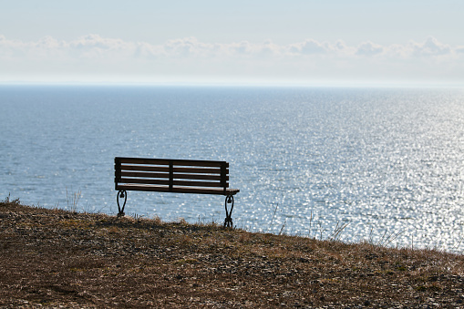Empty bench on cliff before sea background, peaceful and quiet place for thinking alone, loneliness and loss of loved one concept. Pacifying view of marine horizon of Azov sea in Russia, copy space