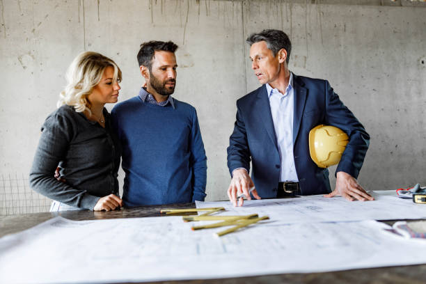 istock Young couple talking to architect about blueprints at construction site. 1433290280