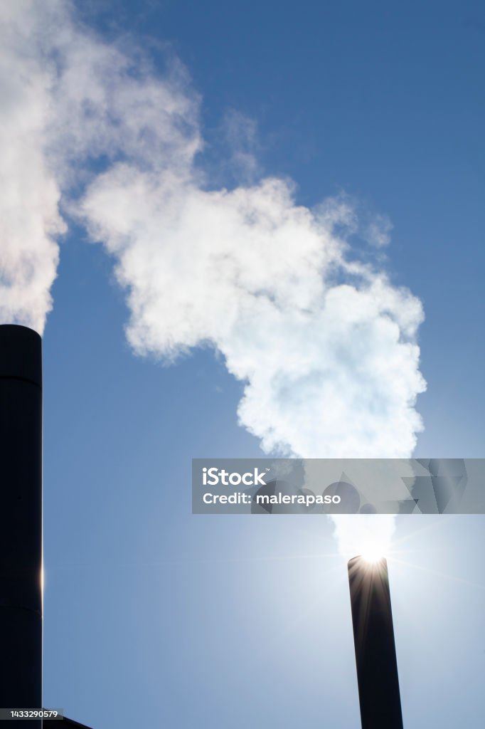 Two chimneys with smoke in the blue sky Air pollution. Steam from the factory pipes. Smog Stock Photo
