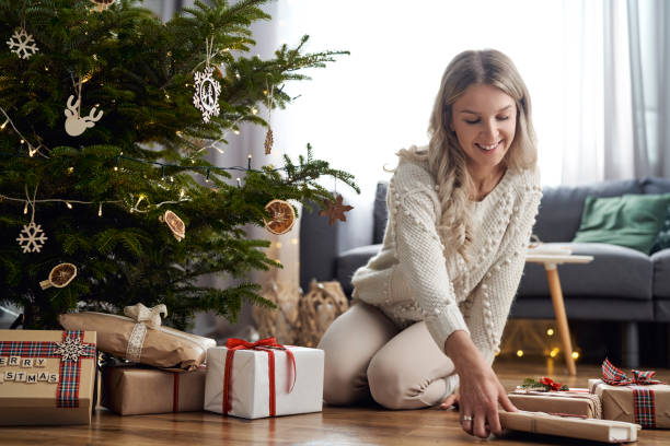 Young caucasian woman putting Christmas gifts under Christmas tree stock photo