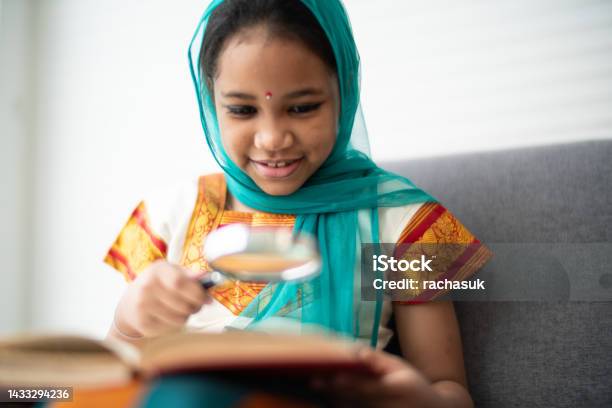 Young Indian Girl Reading A Book Stock Photo - Download Image Now - Child, Sari, Magnifying Glass