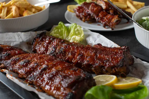 Homemade barbecue meal  on a dining table with marinated spareribs, french fries and salad.