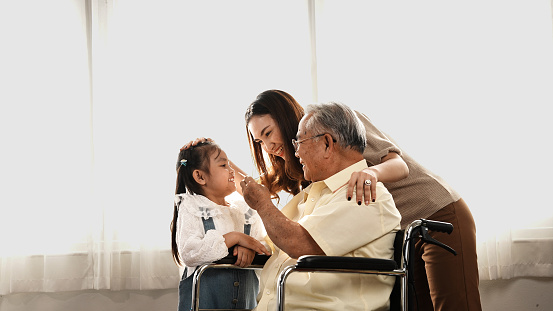 Happy Family Multi-generation Mother and daughter taking care of the senior grandfather in the house, sitting on the wheelchair happiness, Elderly retirement concept.