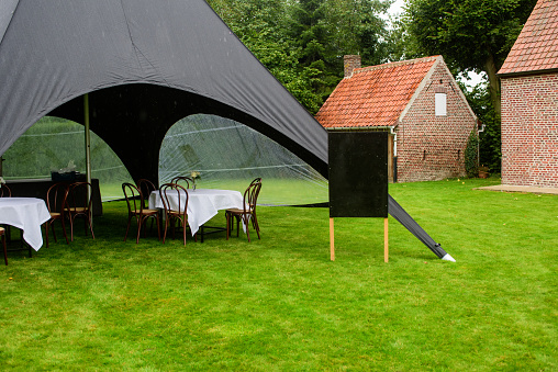 black tent in a garden with dressed tables waiting for people and a black board to writing something on it