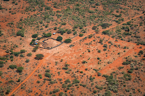 Somewhere in the land of the Masai, Kenya - March 24th 2022. Picture taken from airplane showing a typical Masai tribe farmhouse with suroundings. The tin shacks are used as residential buildings as well as to house lifestock. On the plain across the road, a heard of goats is seen searching for food.