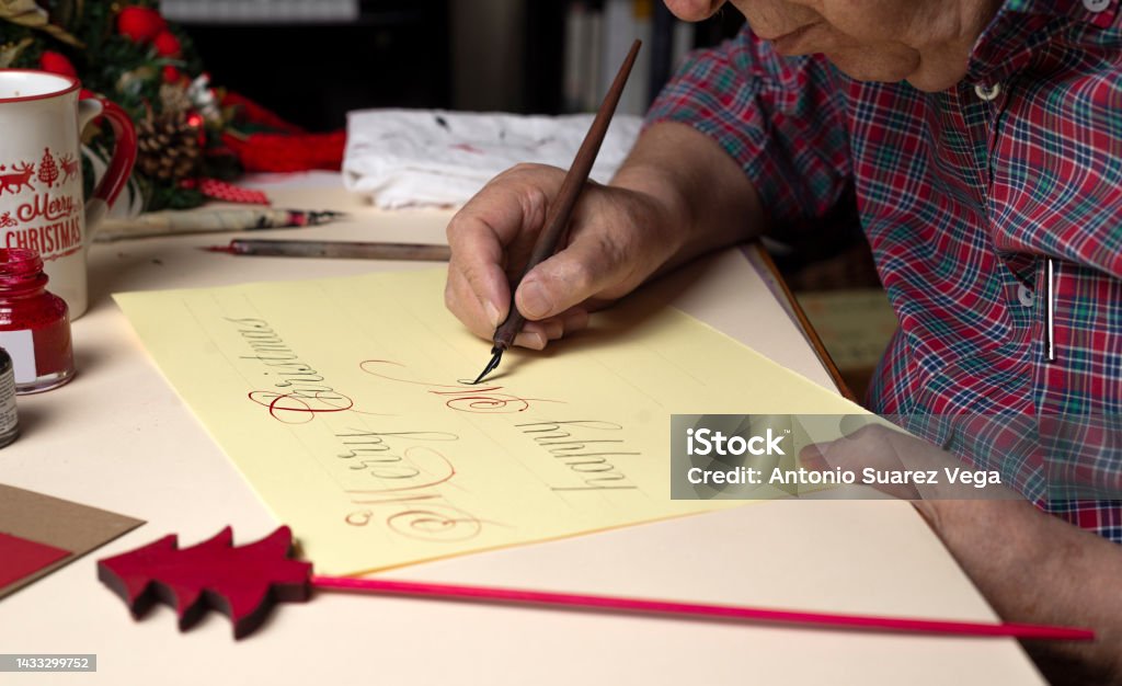 年配の男性がペンとインクと英語の書道でクリスマスカードを書く。手書き書道 - カリグラフィーのロイヤリティフリーストックフォト