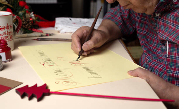年配の男性がペンとインクと英語の書道でクリスマスカードを書く。手書き書道 - inoki antonio ストックフォトと画像