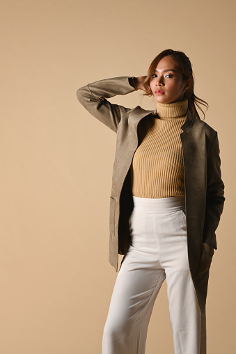 Trendy young woman in brown jacket standing over beige background. Fashion studio photo, Autumn and Winter concept.