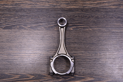 Car engine connecting rod on wooden background