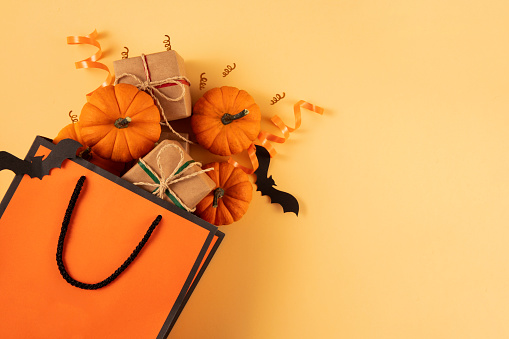 Halloween background with shopping bag gift boxes and pumpkins on orange colored background