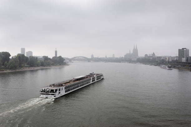 A cruise liner on Rhine river approaches Cologne on a foggy morning. View from Zoobrücke upriver towards Cologne cathedral.