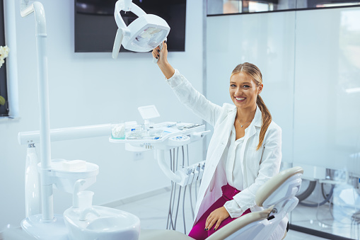 Young female dentist in white coat at workplace. Space for text. Portrait of young female dentist in office. Confident woman dental specialist staying in her office while crossing arms below chest and looking straight