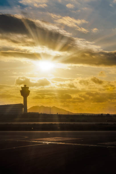 istock Day view of empty runway with airport tower control silhouette and sunrays beaming over puffy clouds. 1433310984