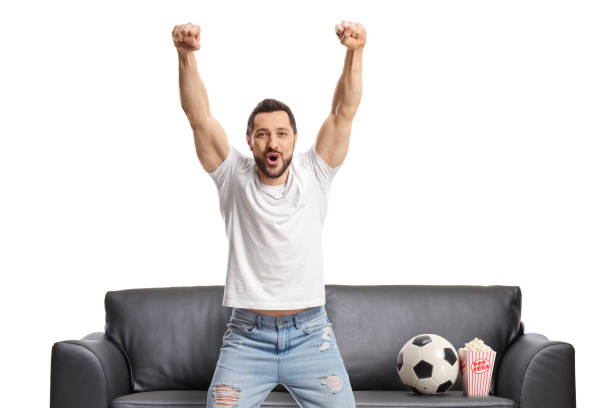 istock Happy young man cheering with a football on a sofa 1433311548