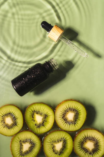 Facial pipette serum black bottle, whey beauty product near fruit kiwi slice in water splash fresh transparent. Vertical stock photo