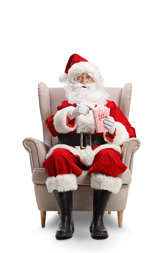 Santa claus sitting in armchair and eating popcorn isolated on white background