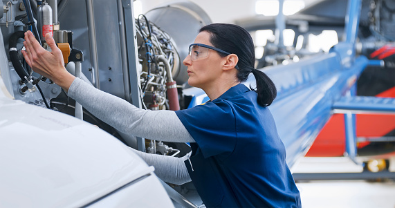 Female airplane mechanic checking helicopter in hangar.