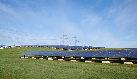 Solar power station, two electricity pylons in the background, Germany.