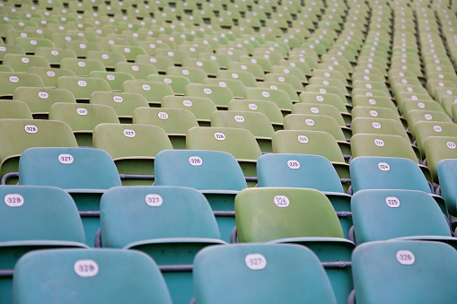 Empty green and turquoise plastic seats on grandstands of outdoor stadium