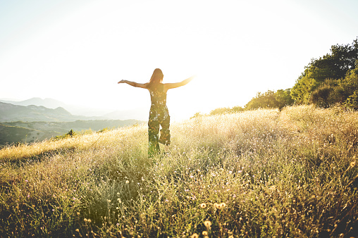 woman hiking a hilly trail. rear view of a young woman in a meadow on golden hour.