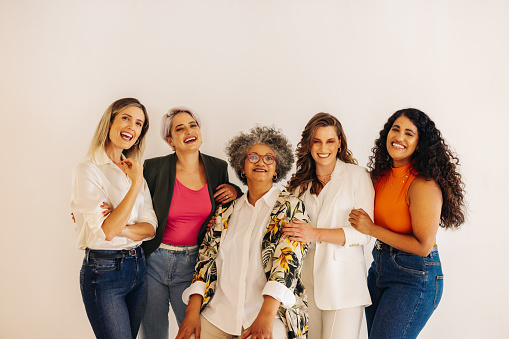 Diverse female entrepreneurs smiling at the camera while standing together in an office. Group of multicultural businesswomen working as a team in a successful all-female startup.