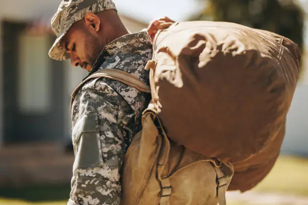 Brave serviceman carrying his luggage outside his home. Rearview of a patriotic American soldier coming back home after serving his country in the military.