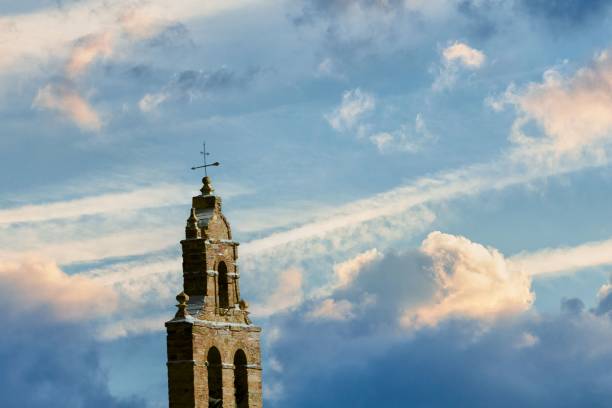 An old church tower against the blue sky with cumulus clouds