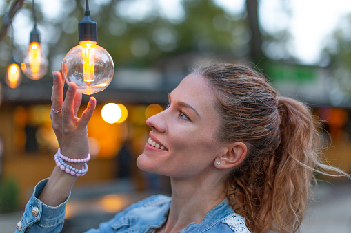Young Caucasian woman holding energy efficient LED string light bulb at outdoors
