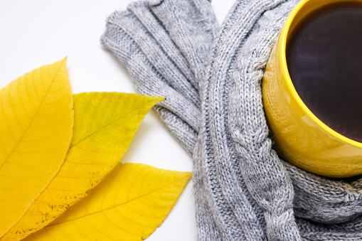Cozy autumn fall composition with yellow leaves and a cup of coffee with a warm cozy knitted pullover.