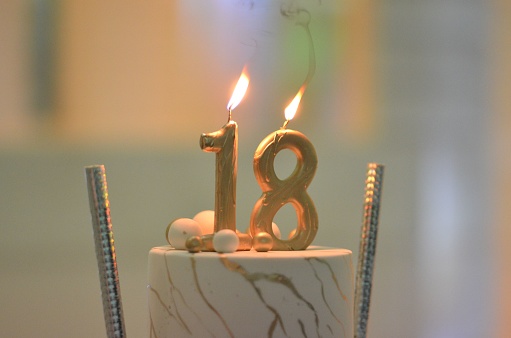 A closeup of a birthday cake with burning candles. 18th anniversary.