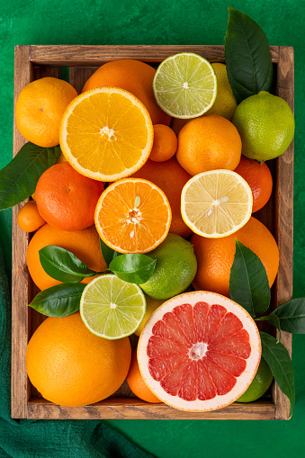 Different citrus fruits with leaves in a wooden box on a concrete background. Healthy food. Top view.