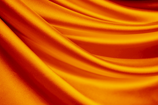 Orange silk satin curtain. Bright luxury background for design. Soft folds. Shiny golden draped fabric.  Wavy lines. Flowing. Fluid, liquid, ripple effect. Valentine, Mother's day, festive. Fiery.