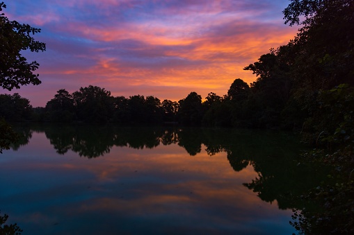 A beautiful view of a pond with silhouettes and reflection at a sunrise with reddish clouds