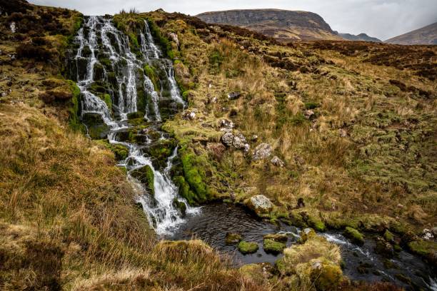 istock Beautiful waterfall flowing down the rocks covered in moss with mountains in the background 1433347850