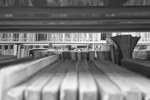 A selective focus shot of books on the shelves in a library seen through blur books in the foreground