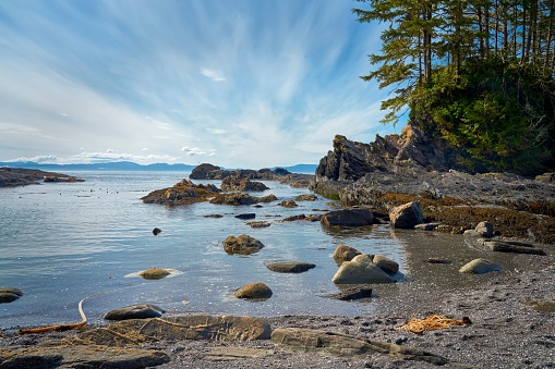 Streaky clouds block out the blue sky over the jagged rocks, beach and ocean water of Botanical Beach, Vancouver Island