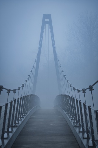 A vertical shot of a footpath on a suspension bridge on a foggy day.
