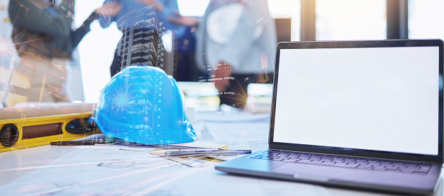 Mockup of architect laptop and planning blueprint, helmet and tools on desk overlay for future architecture building design. Double exposure engineer or construction worker office workplace workspace