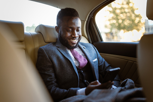 Black businessman texting in the back seat of limousine