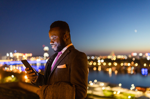 Black businessman texting in front of a beautiful night cityscape