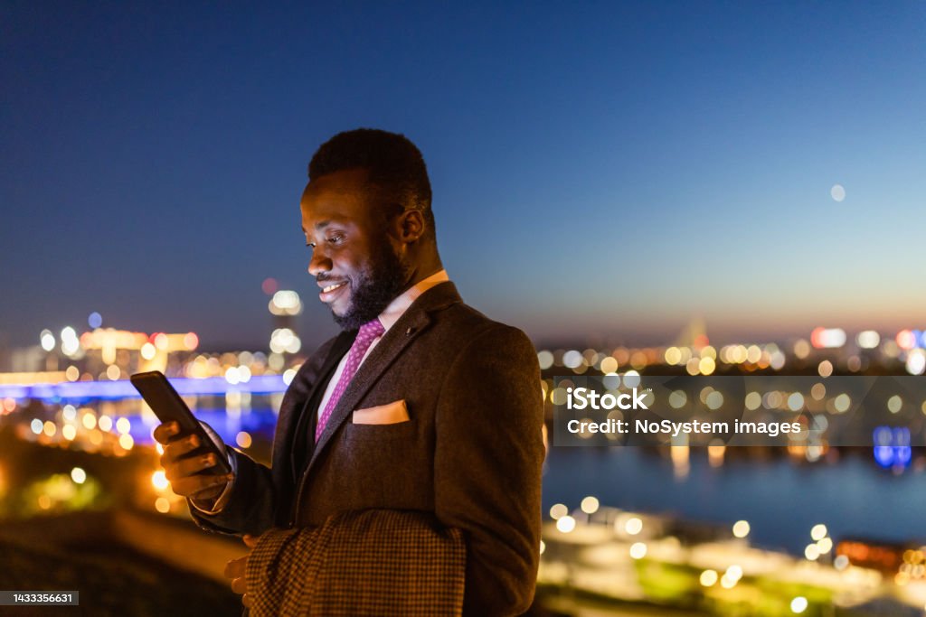Late night text message Black businessman texting in front of a beautiful night cityscape Businessman Stock Photo