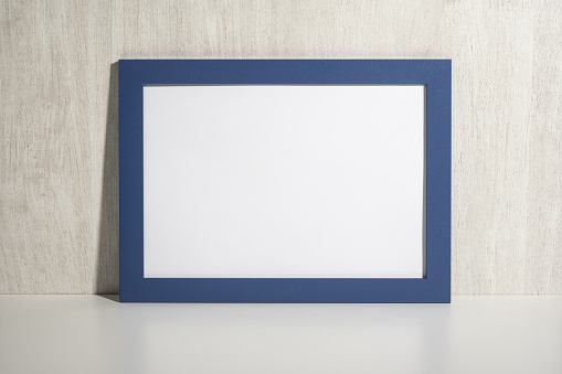 Horizontal blue frame mockup on white shelf, table. Mockup diploma. Certificate, diploma, picture, gratitude blue blank frame mockup. White wooden wall background