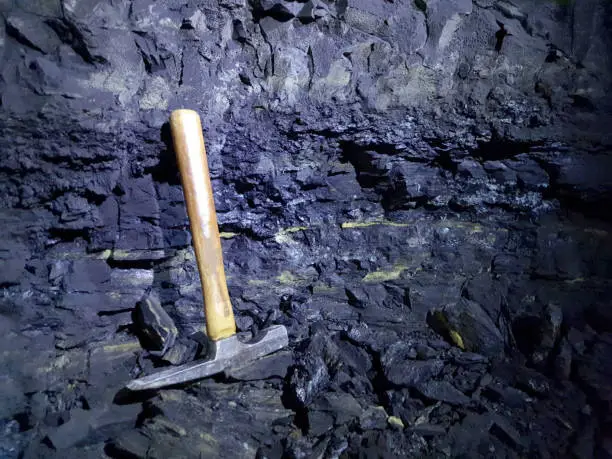 Photo of Geological hammer, isolated on a coal wall. Coal is a fossil fuel, being a non-renewable energy source. It is widely used to generate electricity.