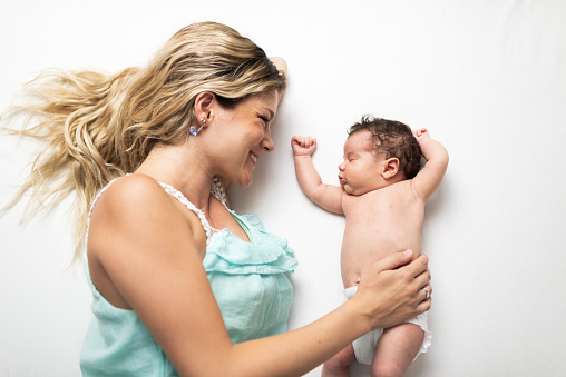 Beautiful young mother and newborn baby in bedroom. High angle view. Baby girl feels love.