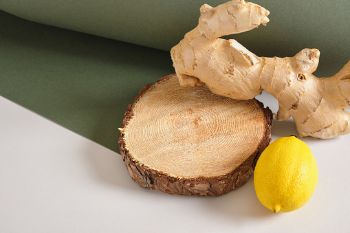 ginger root, lemon and wooden stand on gray and green background, mock up cosmetic background